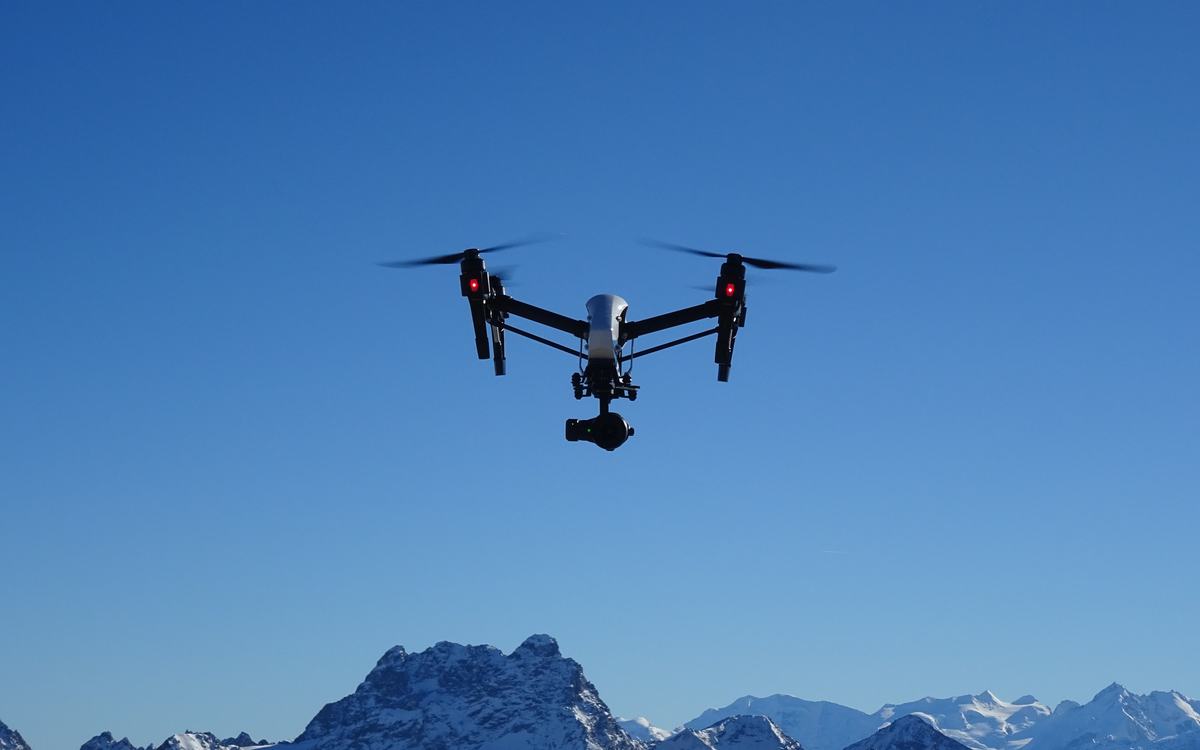 Professional camera drone with a gimbal-mounted camera hovering against a deep blue sky